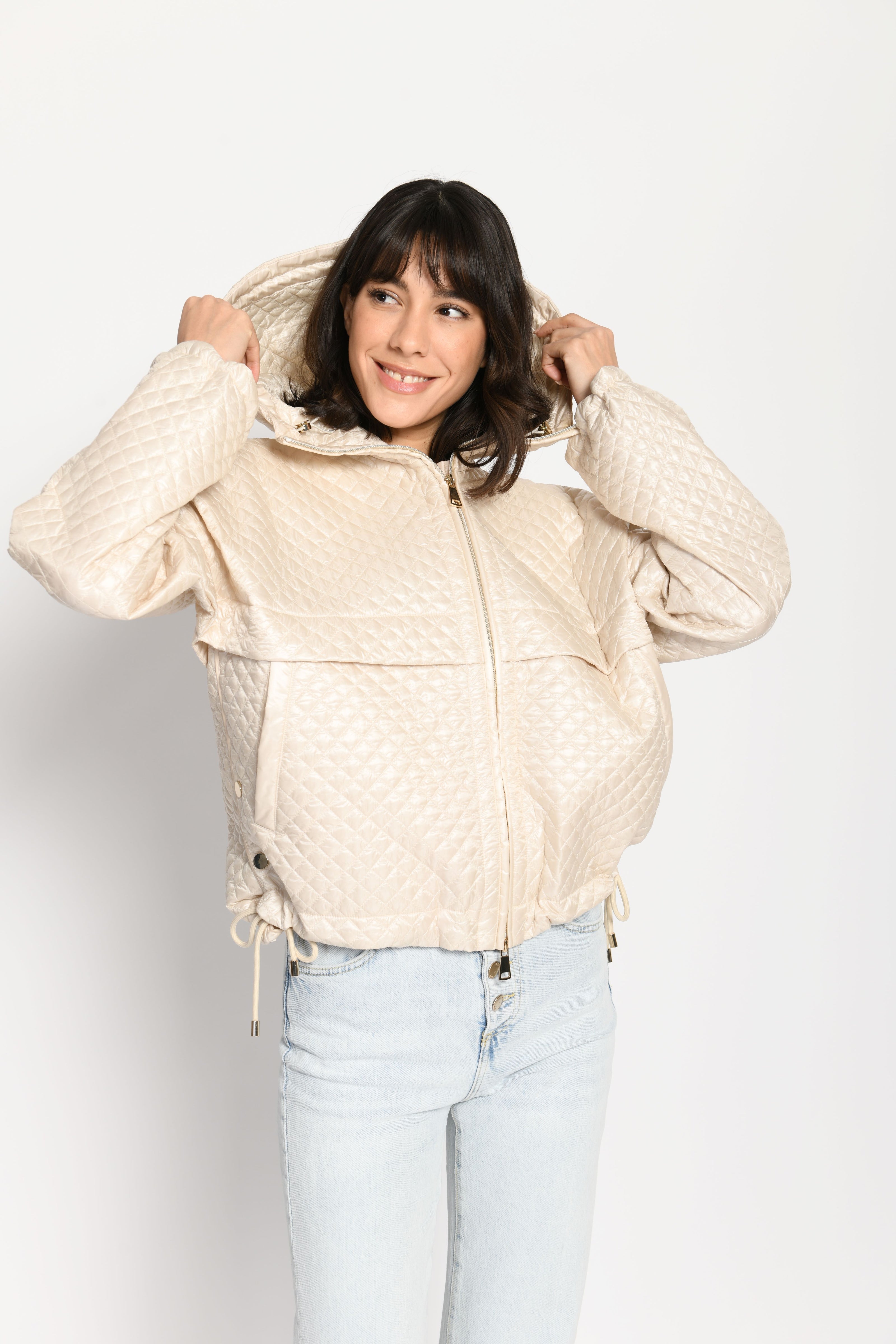 Model trägt beige Oversize-Jacke für Damen mit Sandwich-Steppung zu einer hellblauen Jeans – stehende Pose, Blick nach vorne
