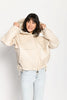 Model trägt beige Oversize-Jacke für Damen mit Sandwich-Steppung zu einer hellblauen Jeans – stehende Pose, Blick nach vorne