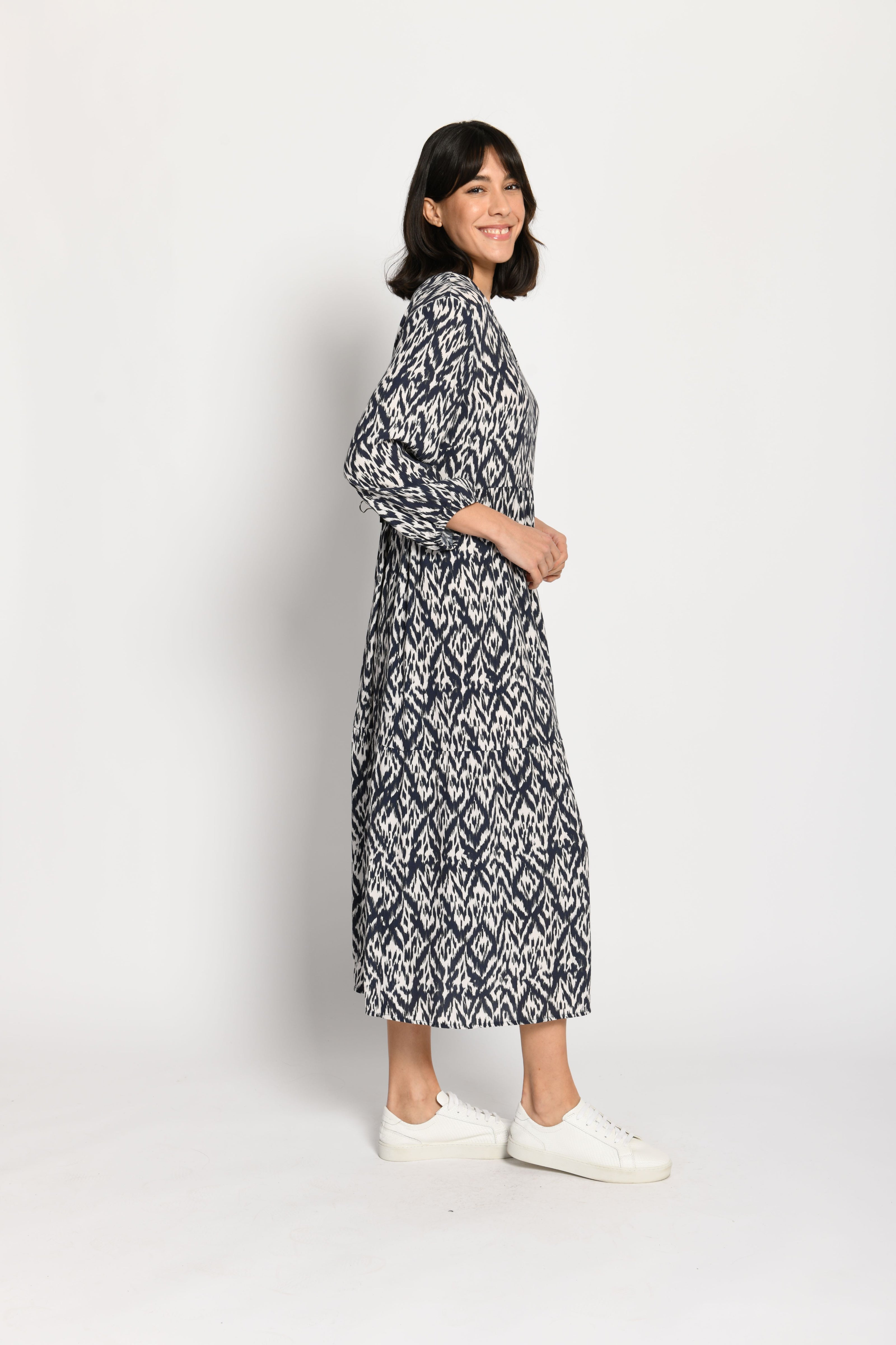Model trägt luftiges Stufenkleid mit langen Ärmeln und tollem Print in den Farben Weiß und Dunkelblau – Seitenansicht