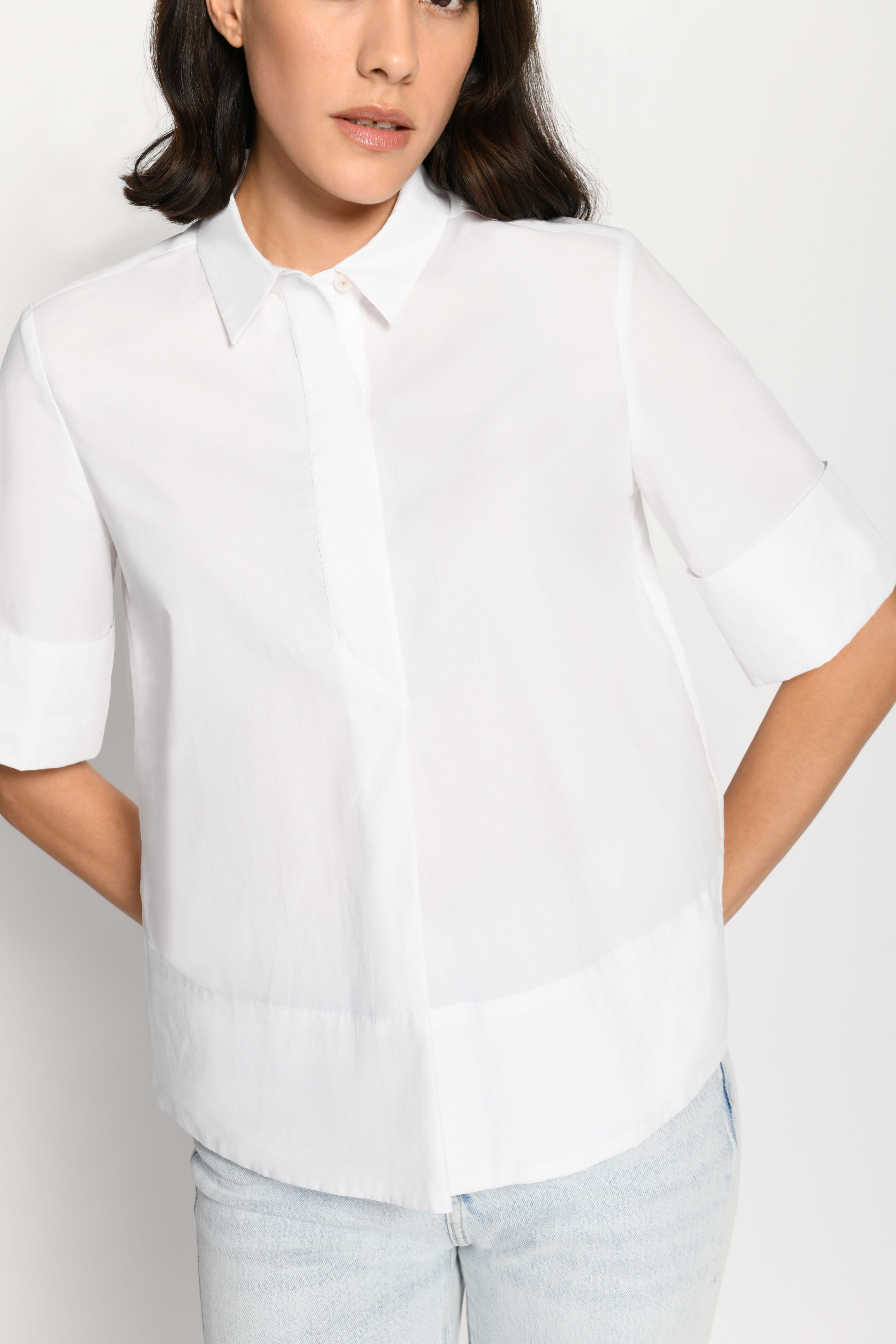 Model trägt kurze kastige Boxy-Bluse in der Farbe Weiß mit kurzen Ärmeln, passend zu einer Jeans – Vorderansicht, stehend