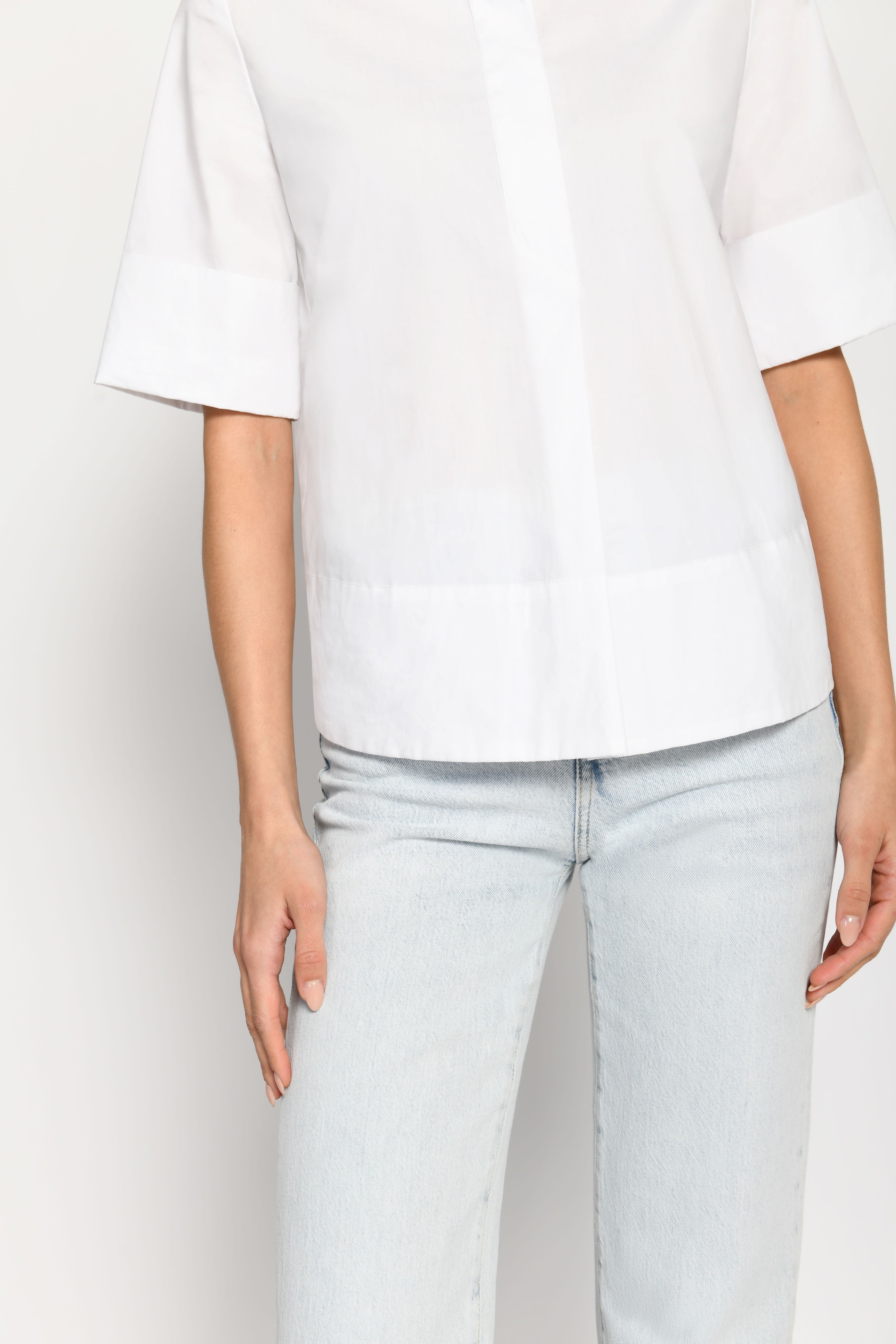 Model trägt kurze kastige Boxy-Bluse in der Farbe Weiß mit kurzen Ärmeln, passend zu einer Jeans – Nahaufnahme