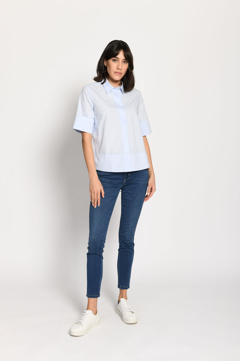 Model trägt kurze kastige Boxy-Bluse in der Farbe Hellblau mit kurzen Ärmeln, passend zu einer Jeans – Vorderansicht, stehend