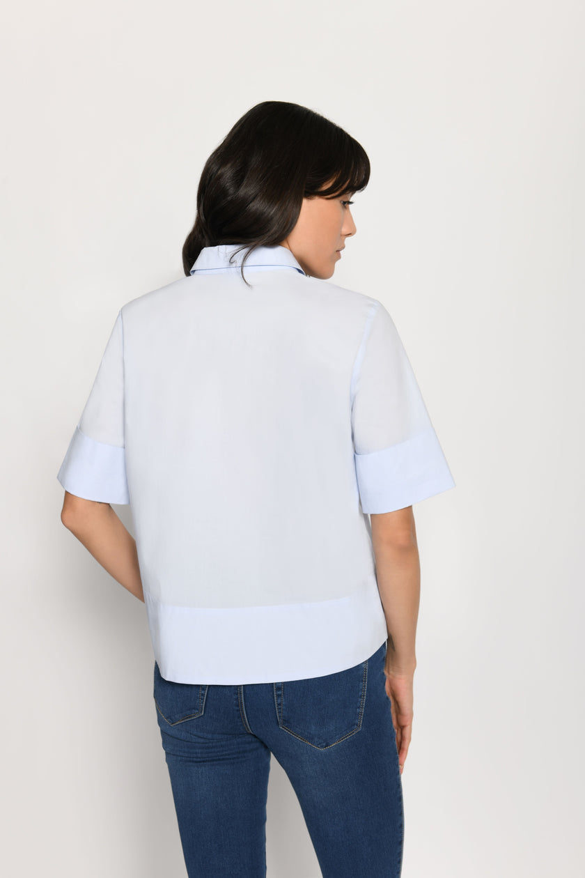 Model trägt kurze kastige Boxy-Bluse in der Farbe Hellblau mit kurzen Ärmeln, passend zu einer Jeans – Rückansicht