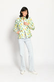 Model trägt leichte Steppjacke für Damen mit kräftigem Zitronen-Print auf weißer Jacke – stehende Pose, Blick nach vorne