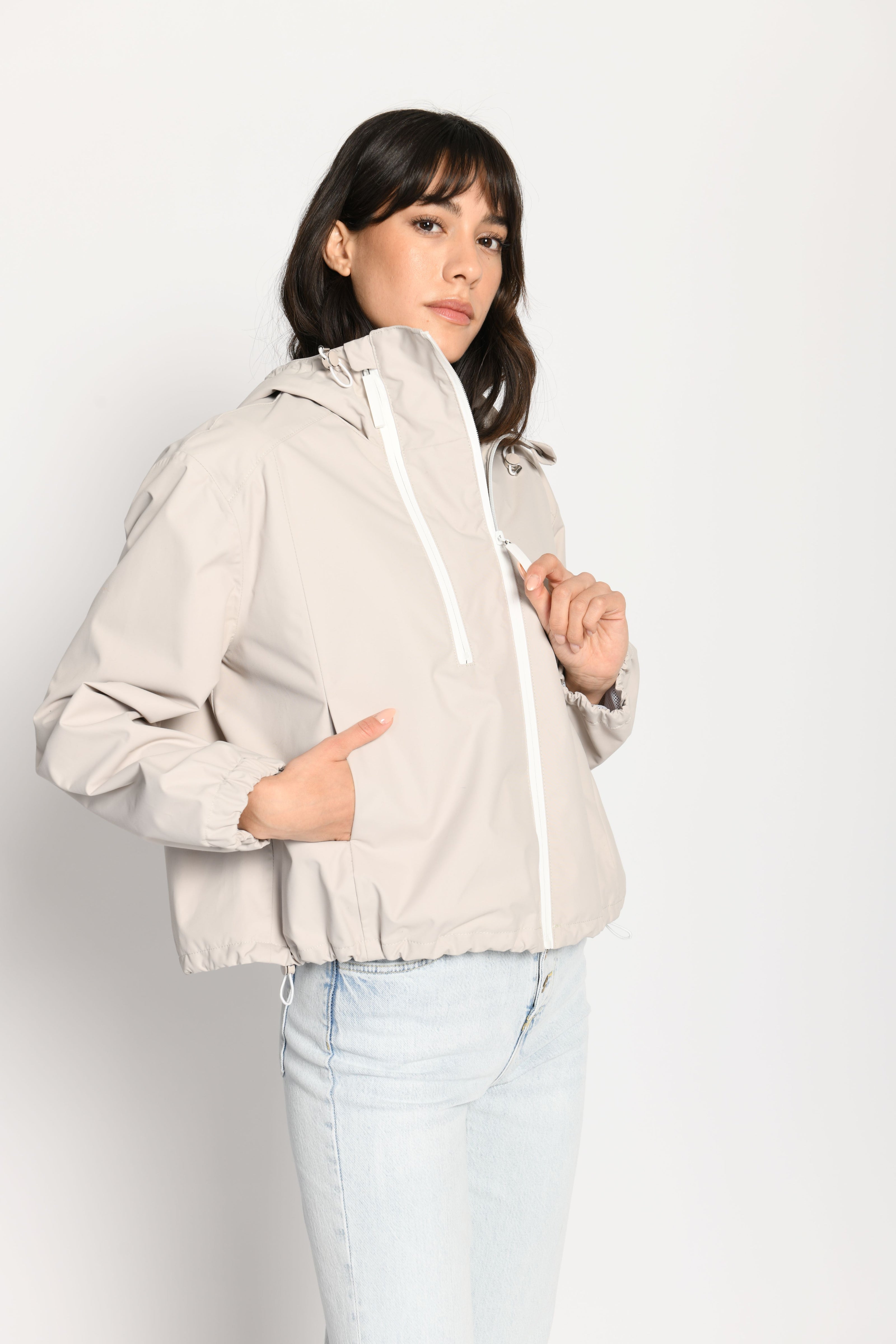 Beigefarbene kurze Outdoor-Kastenjacke mit zwei Reißverschlüssen und Kapuze – Seitenansicht von links