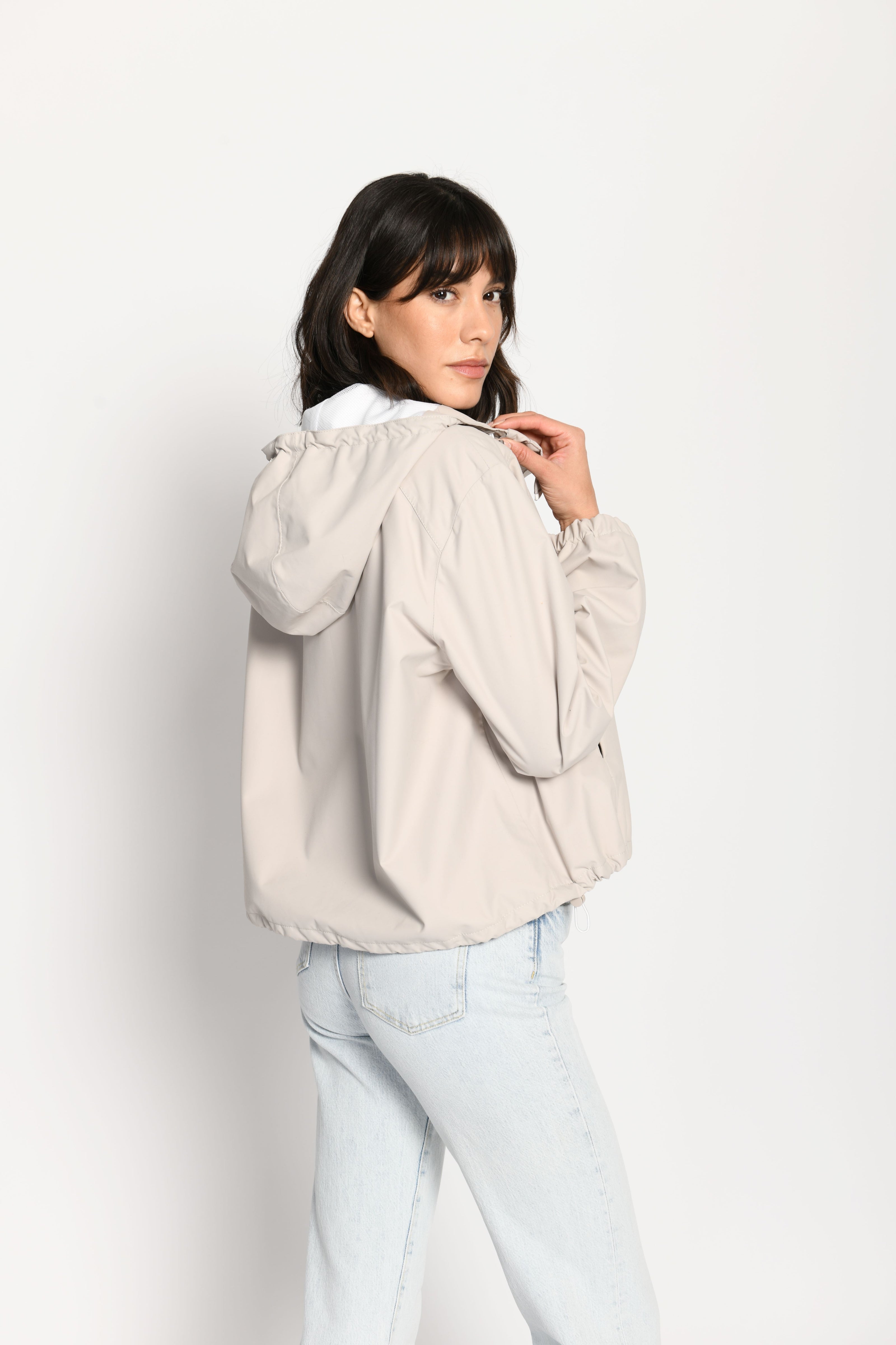 Beigefarbene kurze Outdoor-Kastenjacke mit zwei Reißverschlüssen und Kapuze – seitliche Rückansicht