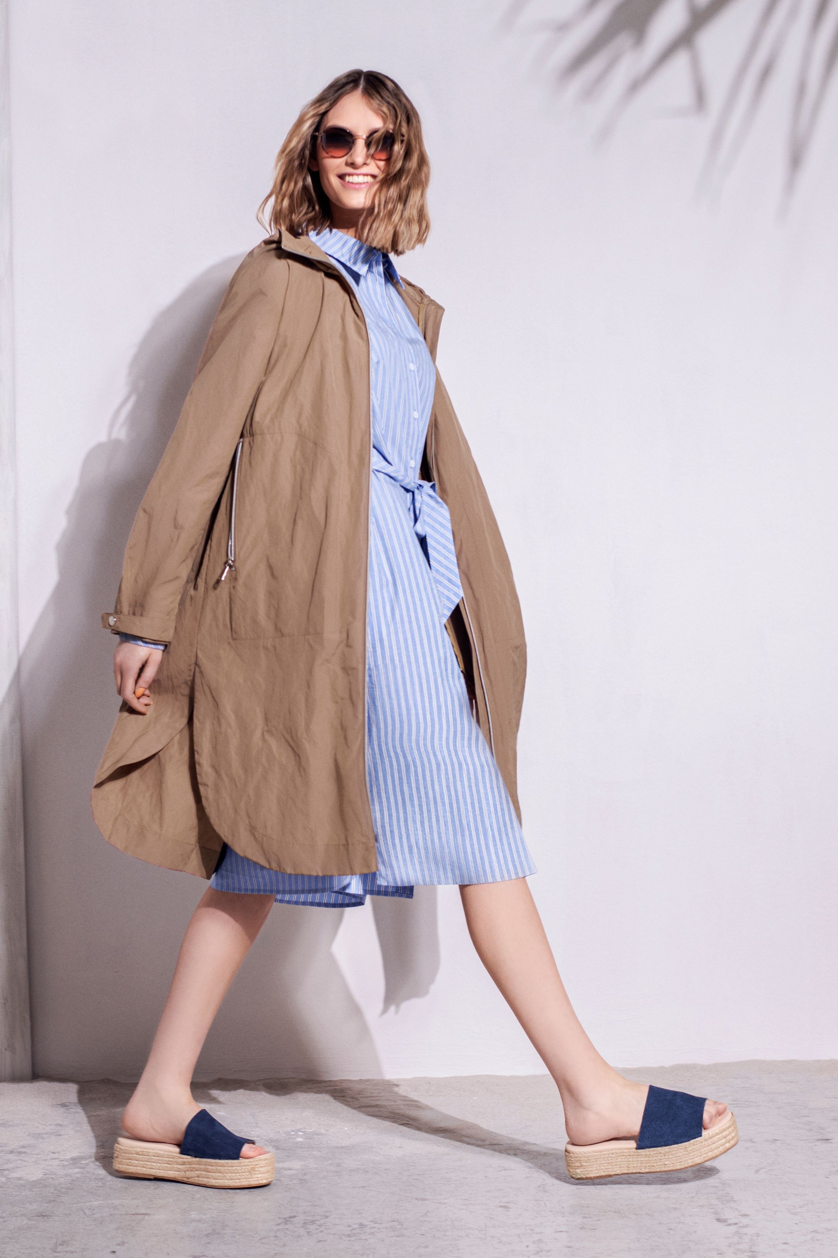 Model trägt leichten braunen Sommerparka, passend kombiniert zu hellblauem Hemdblusenkleid – Seitenansicht von links
