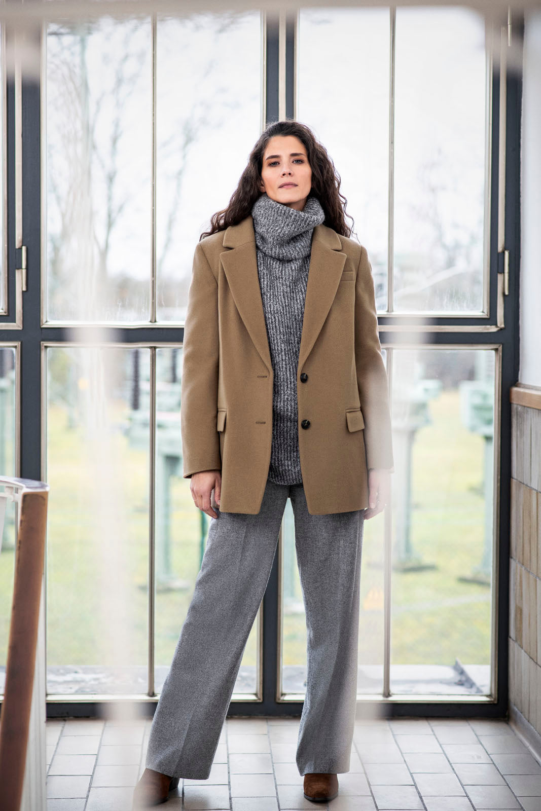Model trägt Outdoor-Blazer in der Farbe Braun, cool kombiniert mit grauem Rollkragenpullover – Vorderansicht, stehend