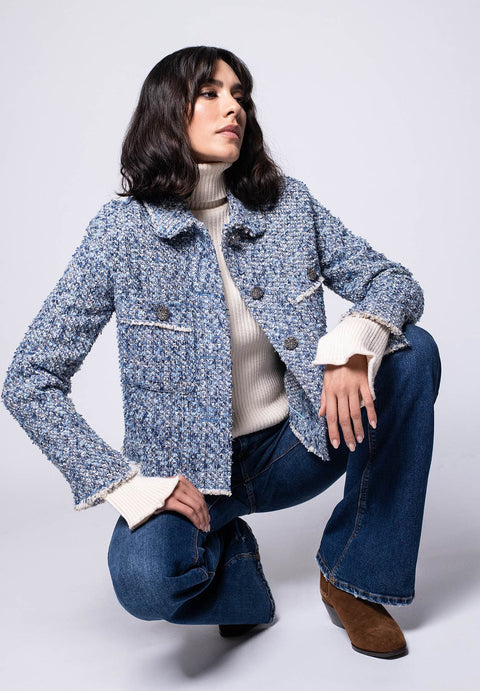 Model trägt kurze Bouclé-Jacke in hellen Farben mit Fransen und Statement-Knöpfen zu Jeans.