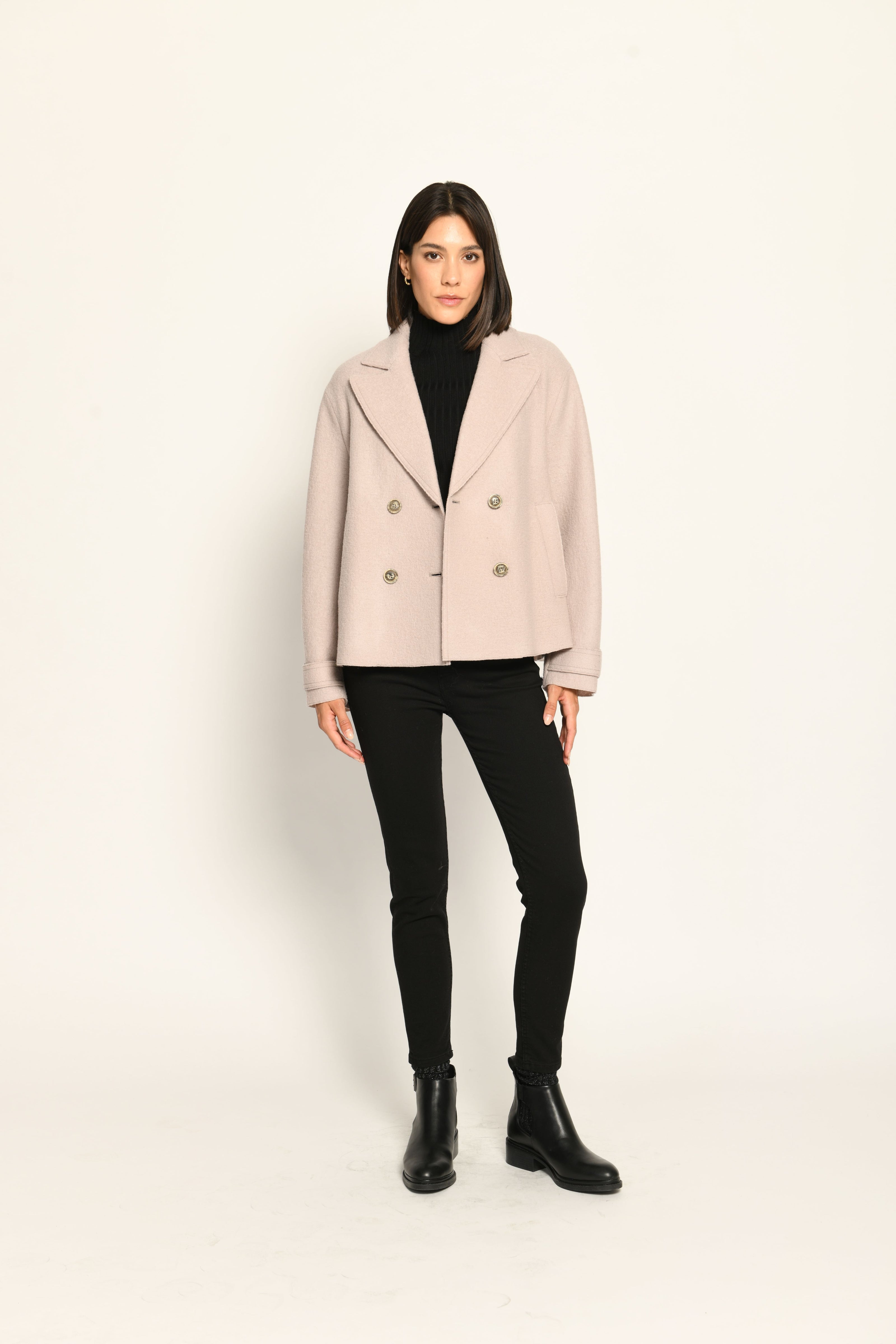 Beige Damenjacke im Caban-Stil mit Reverskragen und zweireihigem Knopfverschluss, kombiniert zu schwarzer Hose.