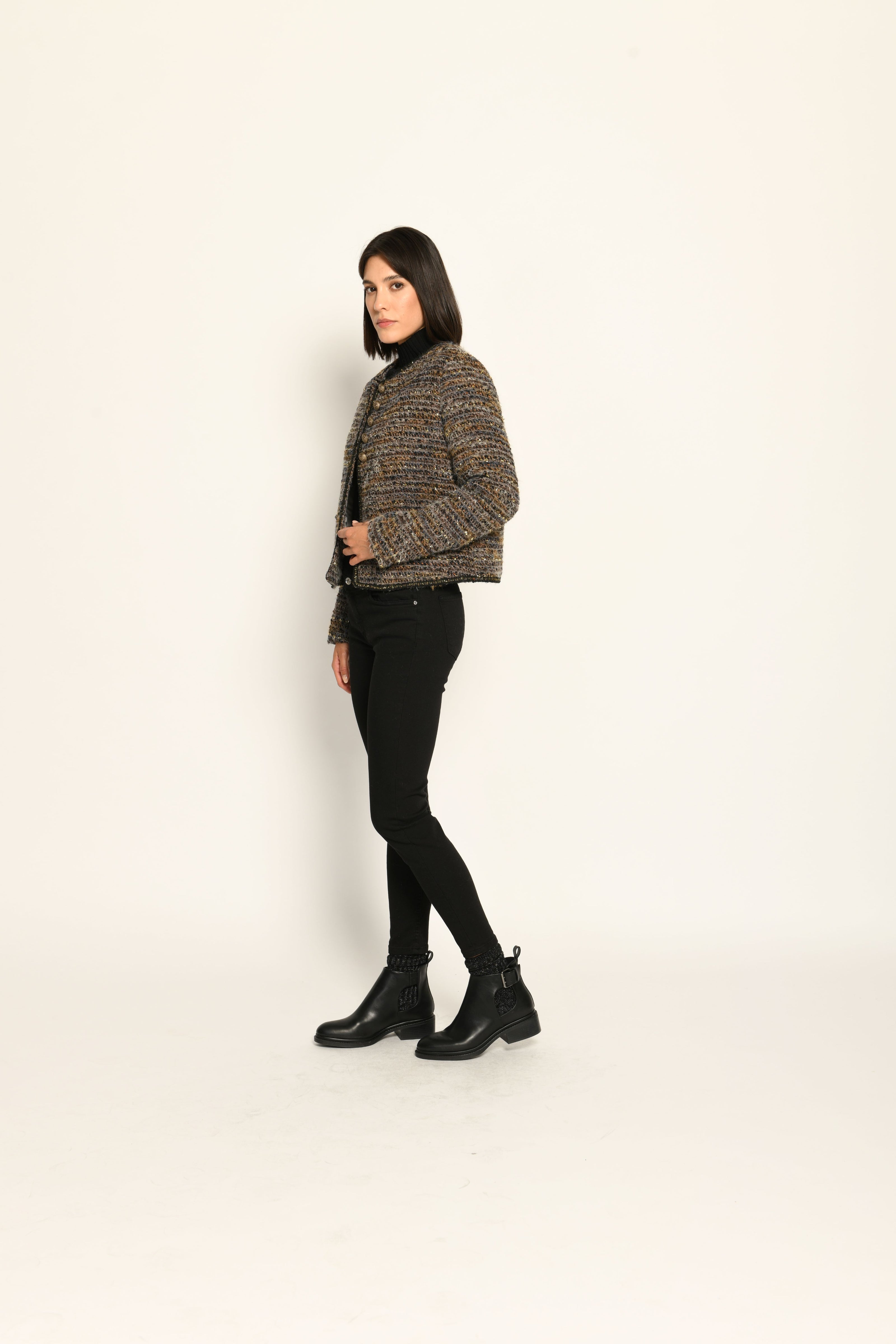 Model trägt Kurzjacke aus Bouclégewebe mit Glanzgarn und Schmuckborte zu einer schwarzen Jeans – Seitenansicht links