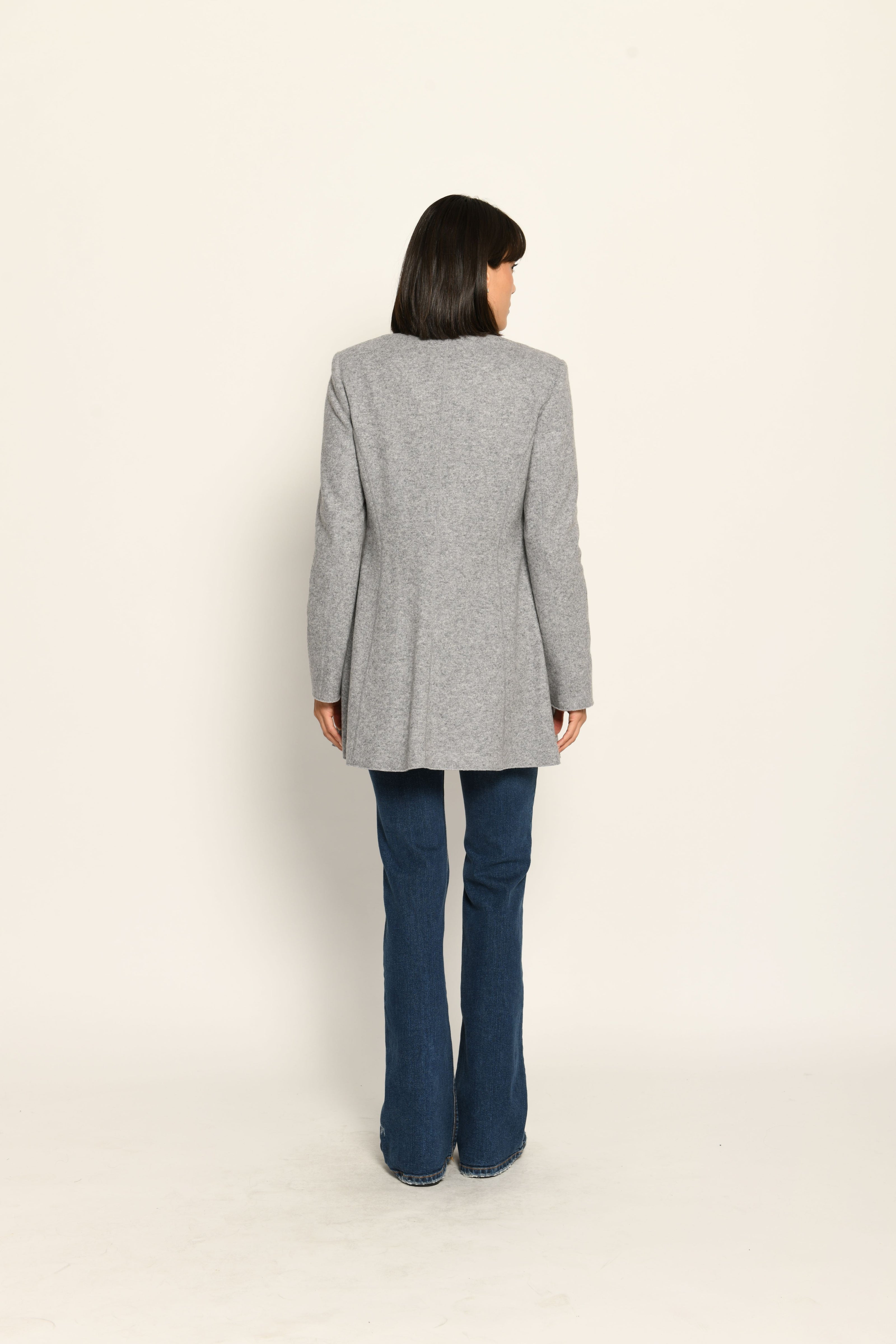 Model trägt grauen taillierten Gehrock aus Wolle mit aufgestelltem Kragen, lässig kombiniert zu Jeans – Rückansicht