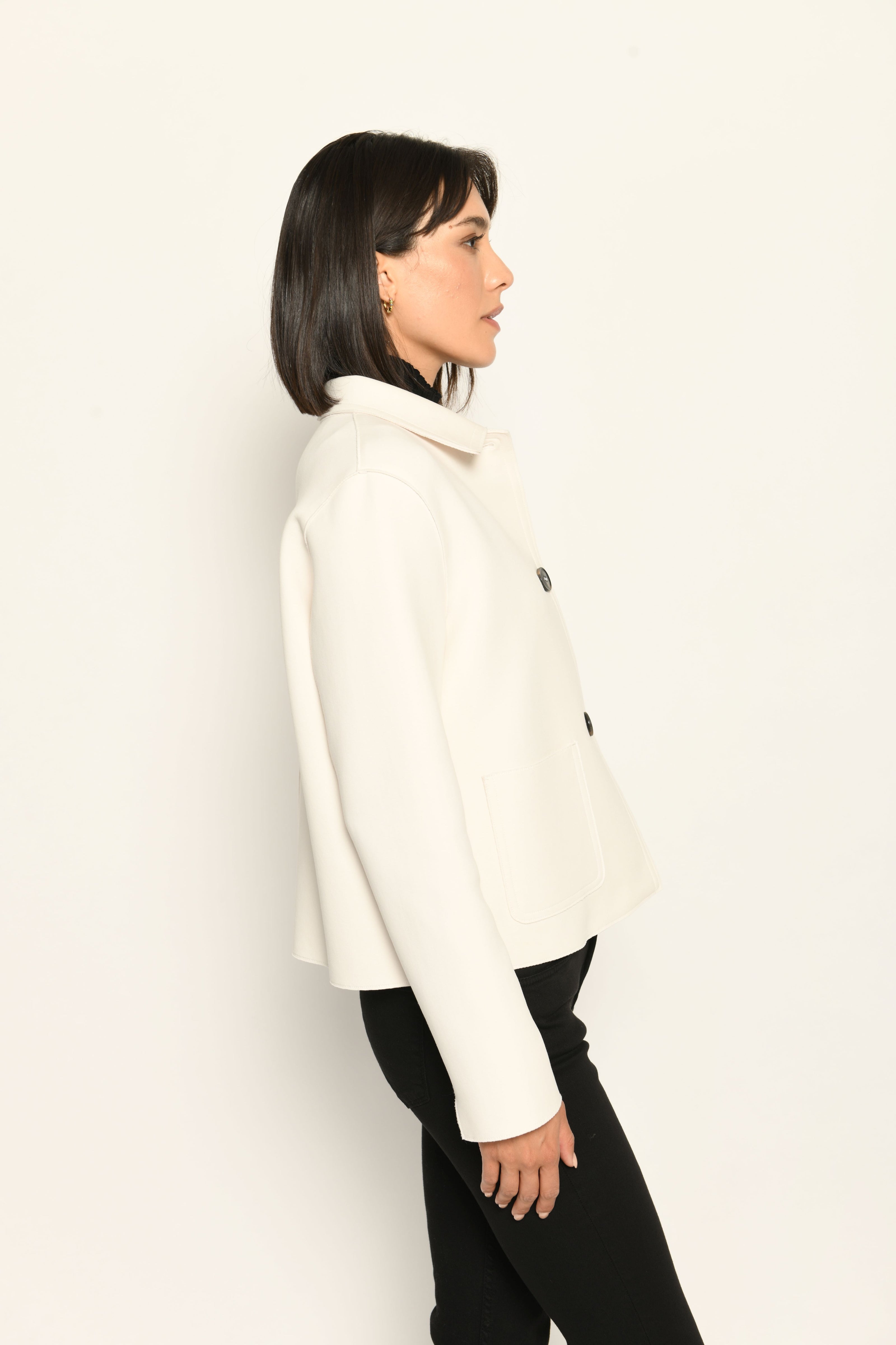 Model trägt weiße Kastenjacke für Damen aus Scuba mit schwarzen großen Knöpfen und aufgesetzten Taschen – Profilansicht