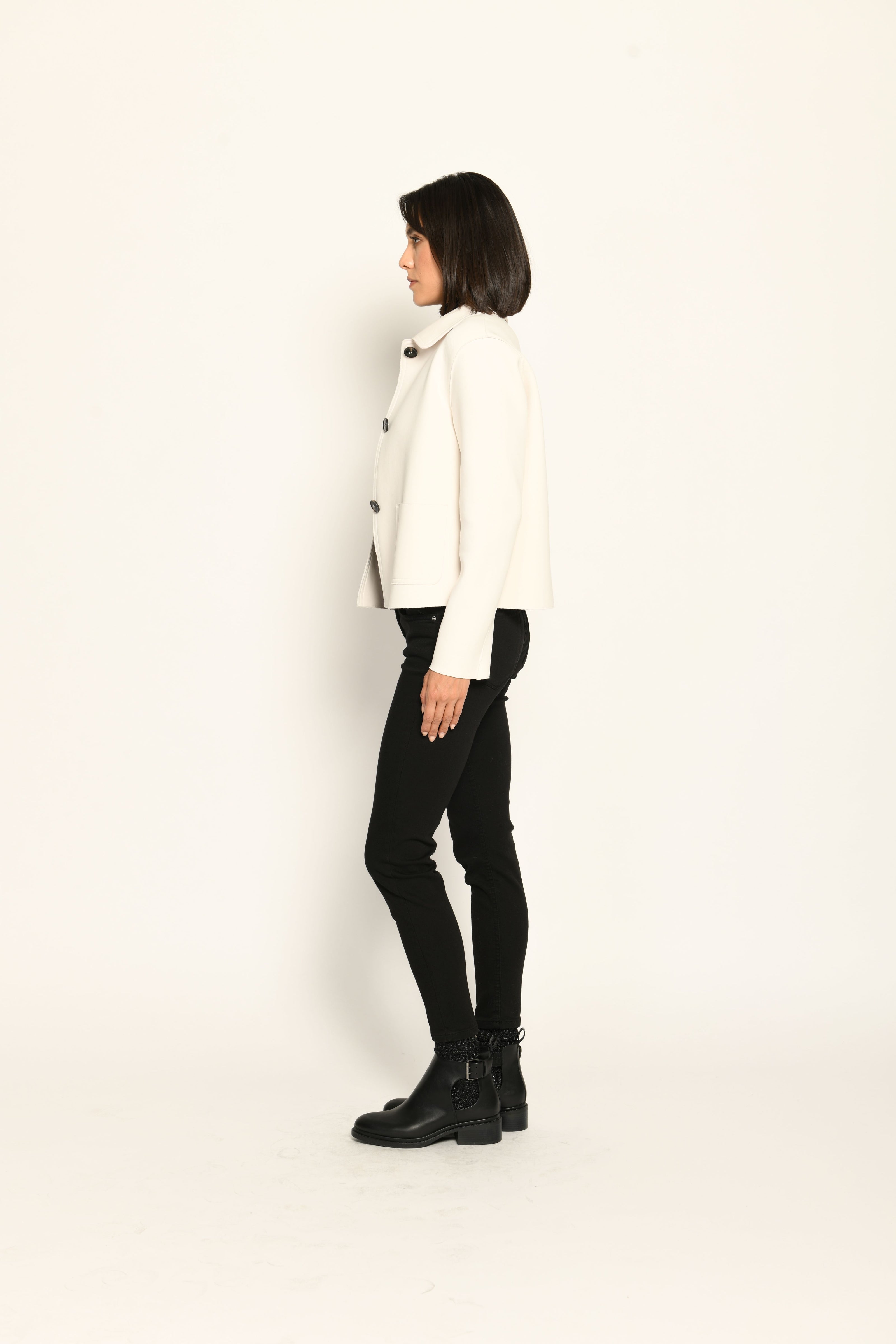Model trägt weiße Kastenjacke für Damen aus Scuba mit schwarzen großen Knöpfen und aufgesetzten Taschen – Seitenansicht