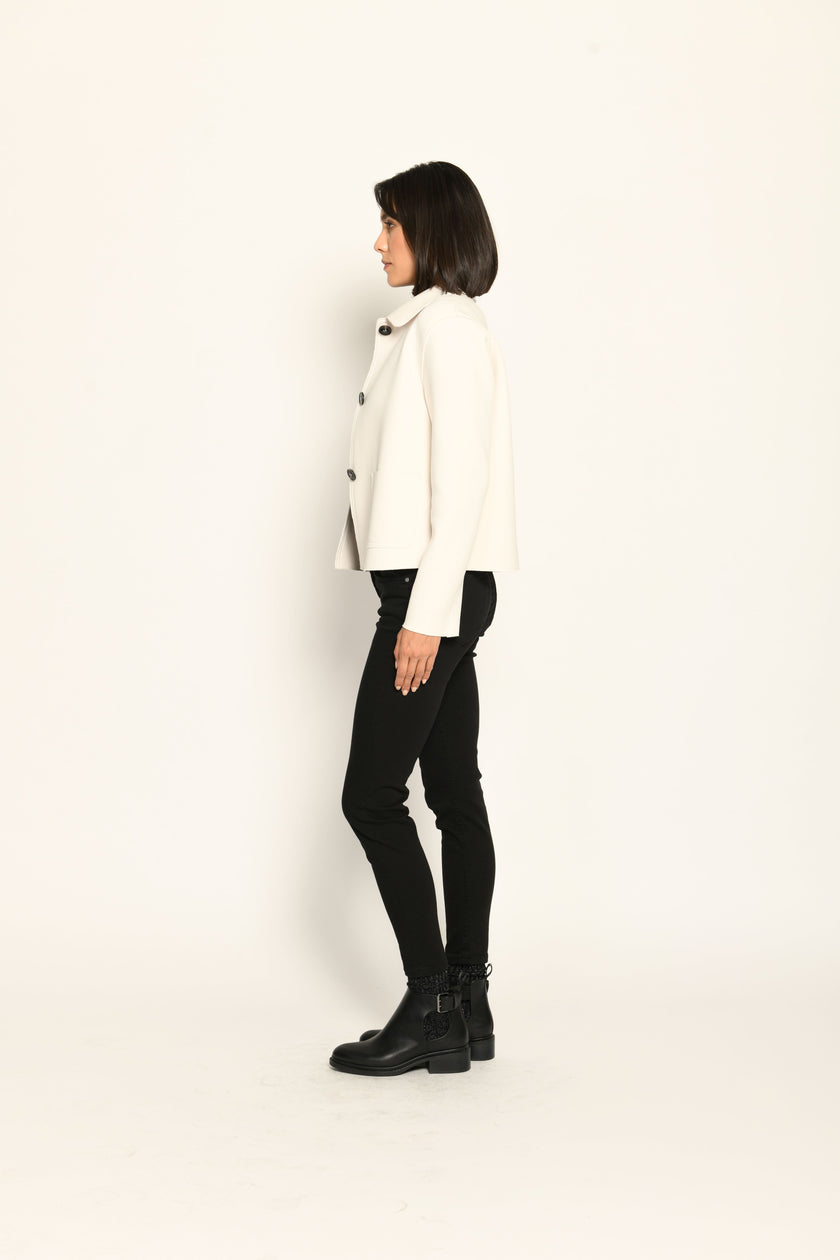 Model trägt weiße Kastenjacke für Damen aus Scuba mit schwarzen großen Knöpfen und aufgesetzten Taschen – Seitenansicht