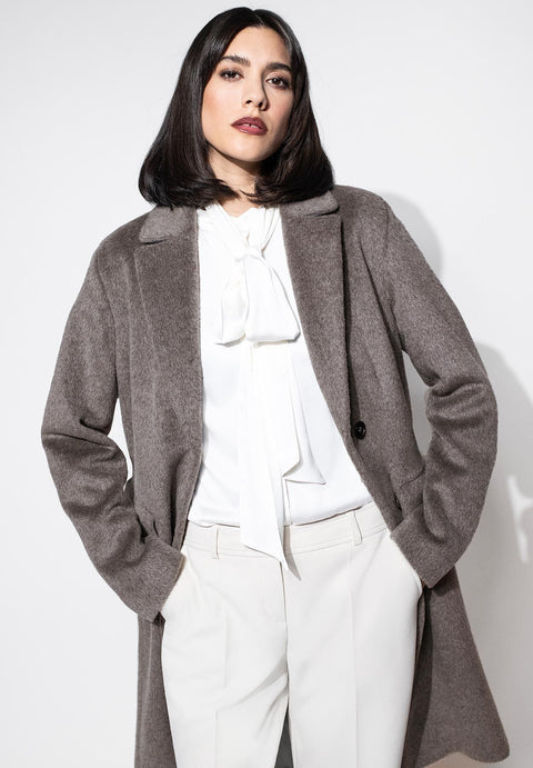 Mantel für Damen aus weicher Flauschware mit Reverskragen, kombiniert mit weißer Stoffhose und Schluppenbluse. 