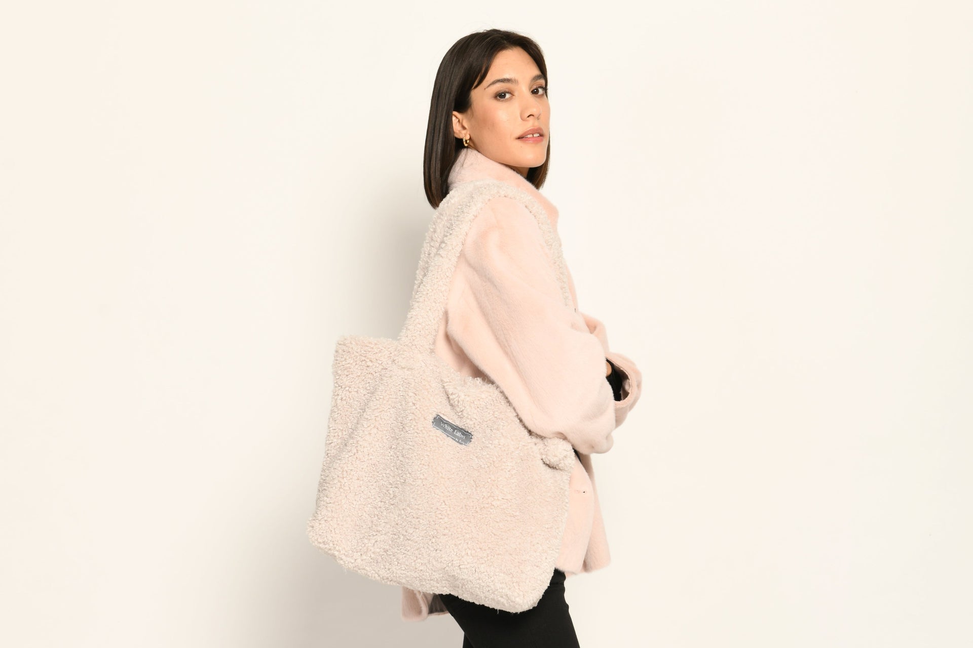 Model trägt Umhängetasche aus Webpelz in der Farbe Creme mit Reißverschluss und zwei langen Henkeln – Seite