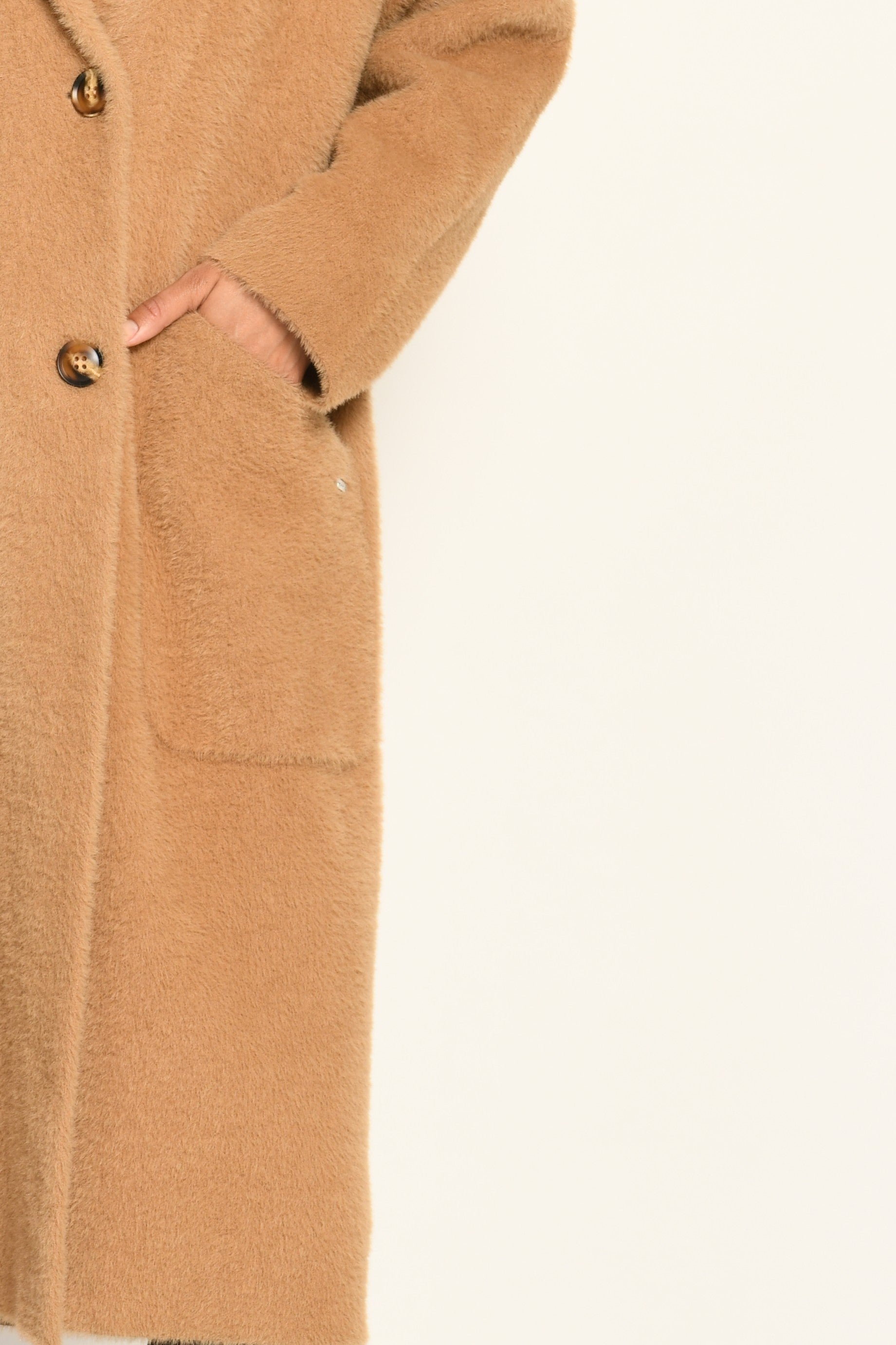 Detailaufnahme zeigt linke Seite des braunen Strickmantels inklusive Knopfleiste und aufgesetzter Tasche.