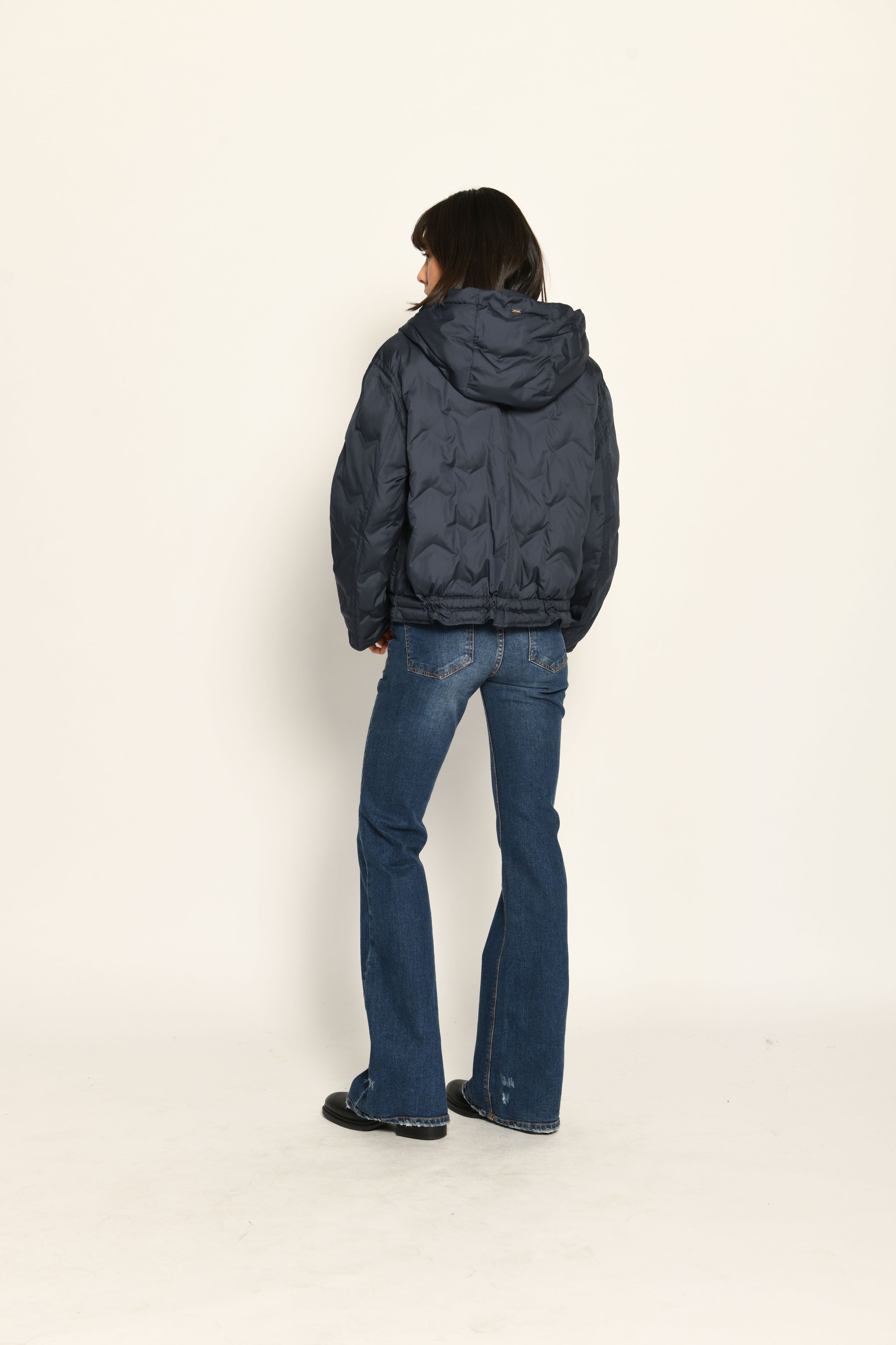 Model trägt sportive dunkelblaue Steppjacke für Damen mit Kapuze zu dunkelblauer Jeans – Rückansicht