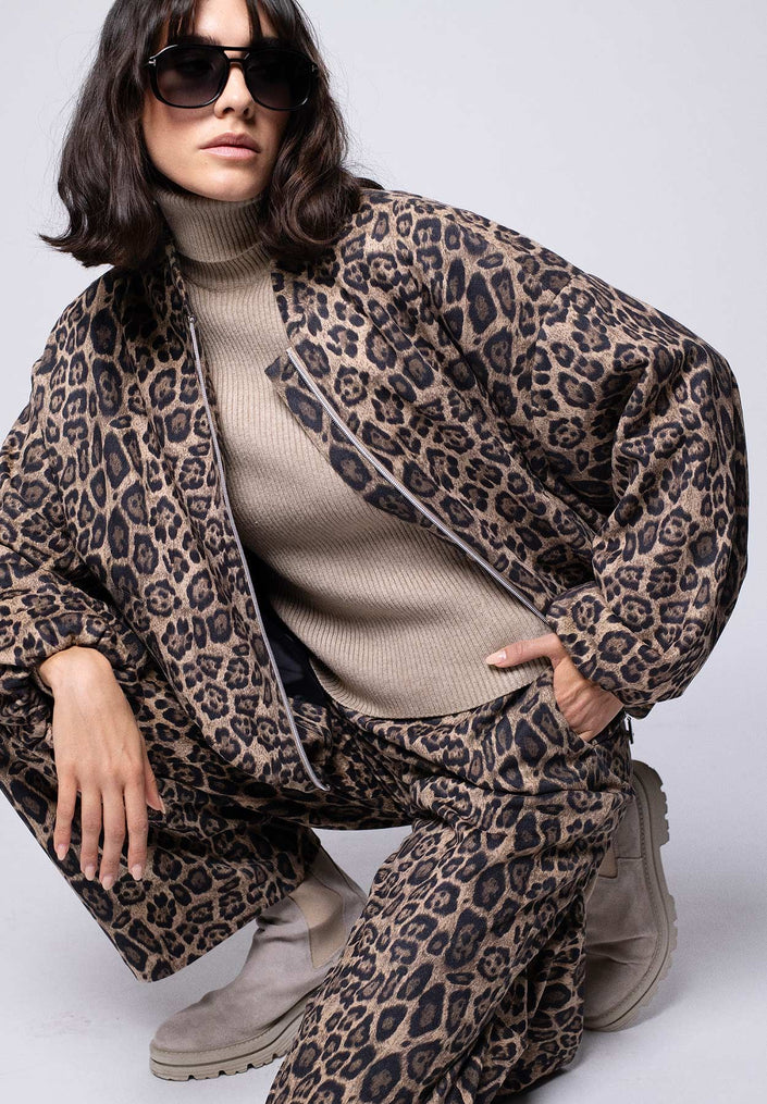 Zweiteiler im Leo-Print für Damen, bestehend aus lässigem Blouson und softer, weiter Hose – Model kniet.